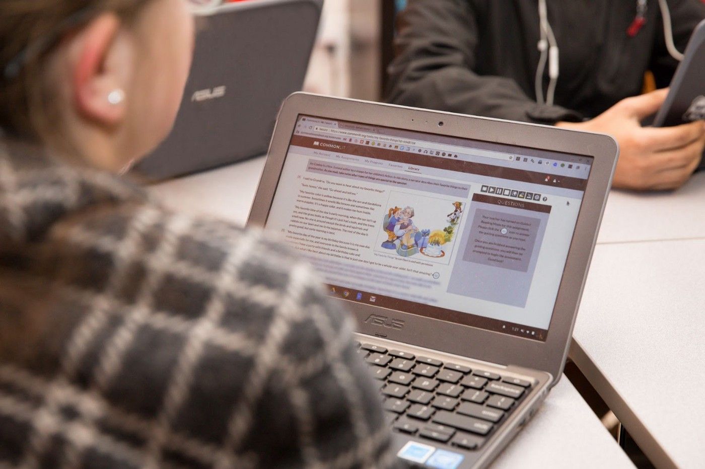 A student sitting at a table and looking at a CommonLit lesson on her computer. 