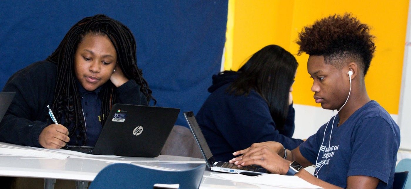 Two students sitting at a table and working on their computers. 