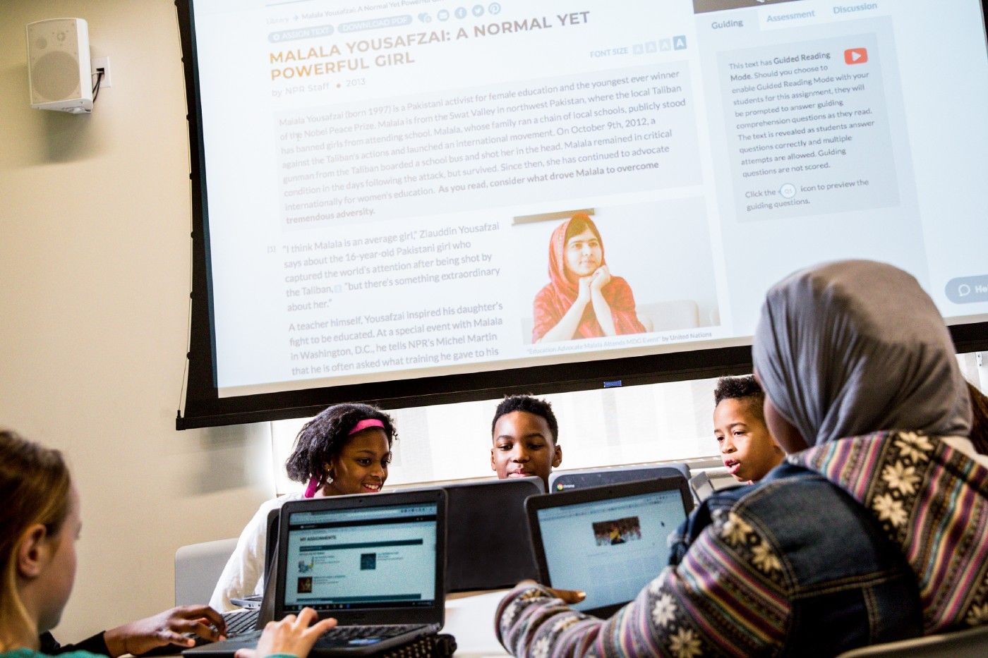 Students gathered at a table while reading CommonLit texts on their laptops.