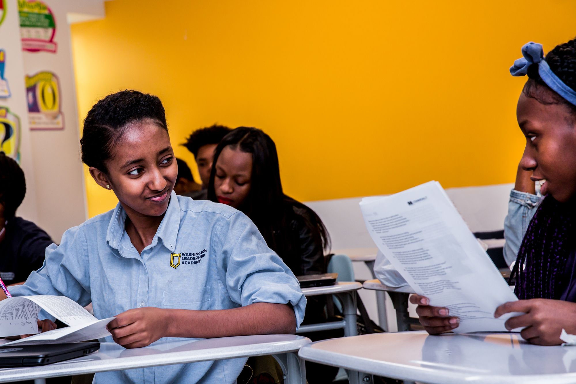 Two students make eye contact while holding CommonLit papers. 