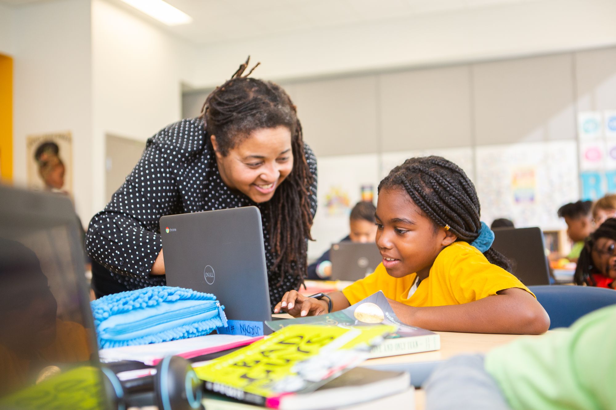 A teacher helping a student with her work on her laptop.