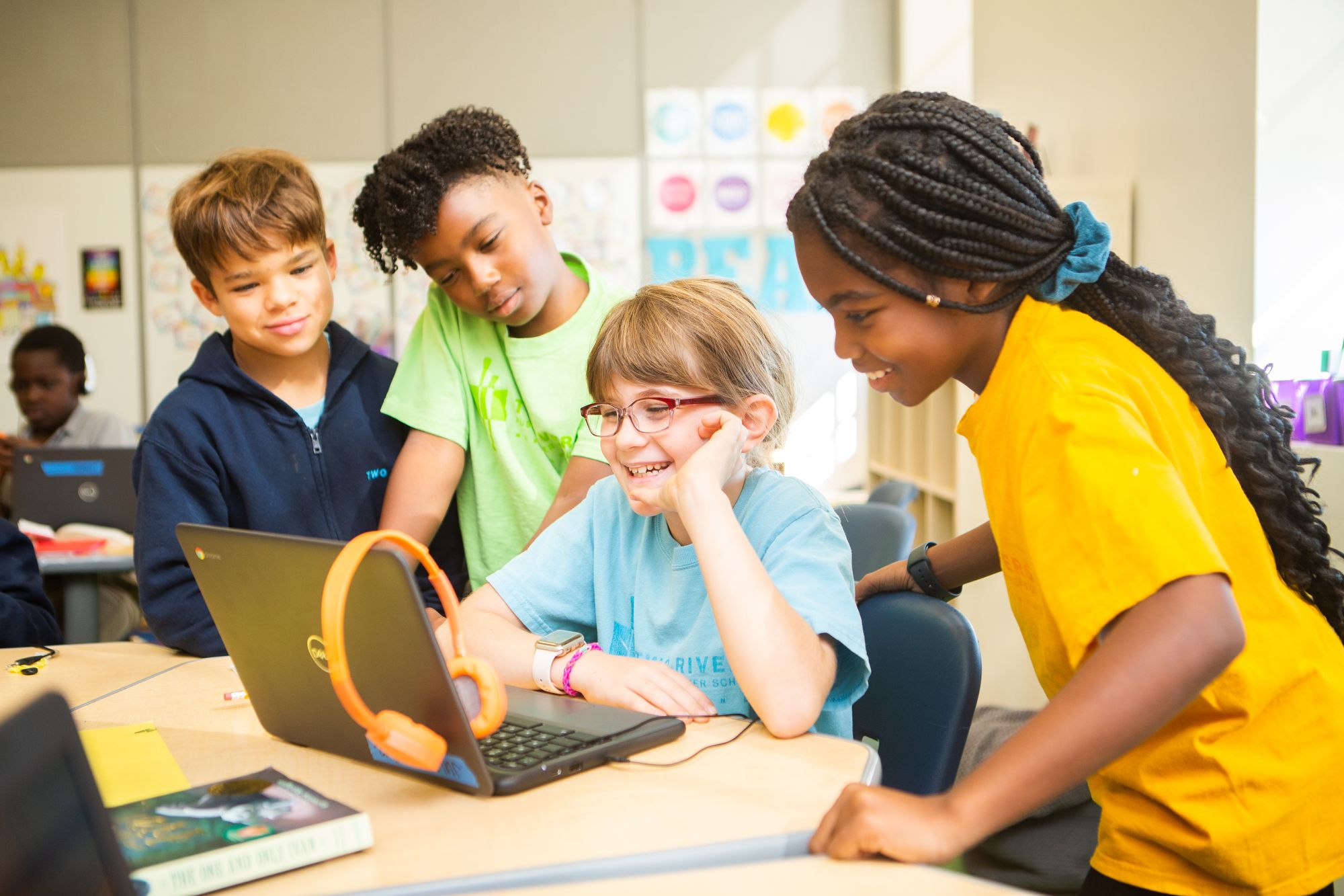 Kids are smiling as they crowd around a laptop and work on a CommonLit lesson