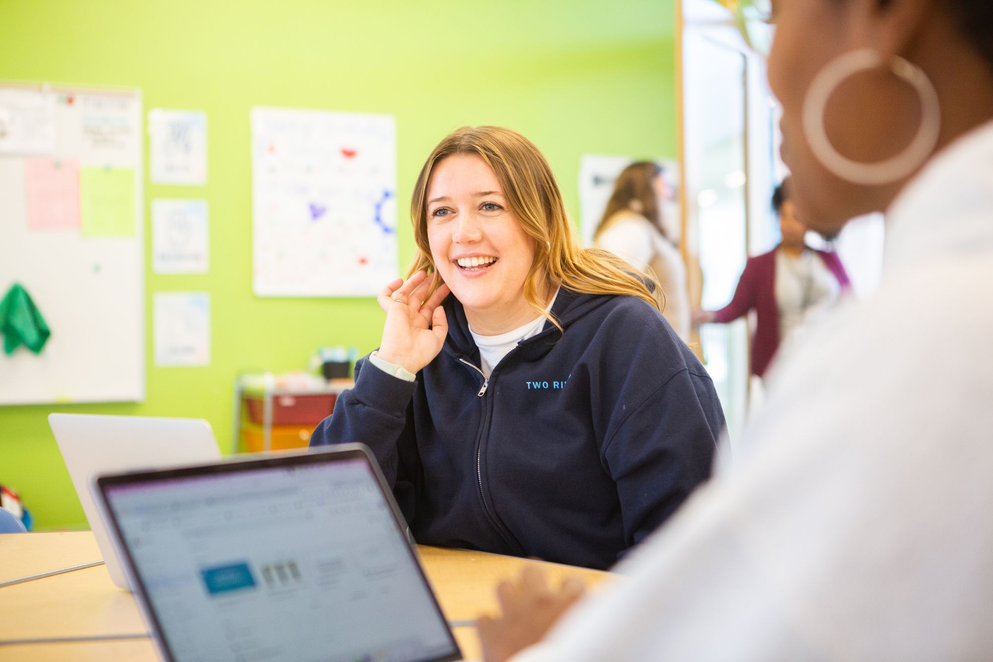 A teacher smiles in conversation with another teacher about CommonLit's seamless digital program.