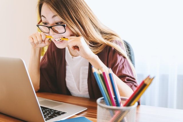 Mujer sentada en su escritorio mirando su computadora y mordiendo un lápiz demuestra que está estresada 