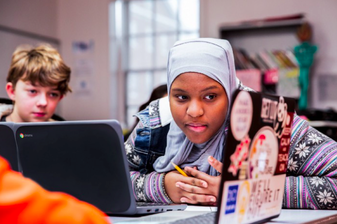 Two students sitting at a table and looking at a computer screen.