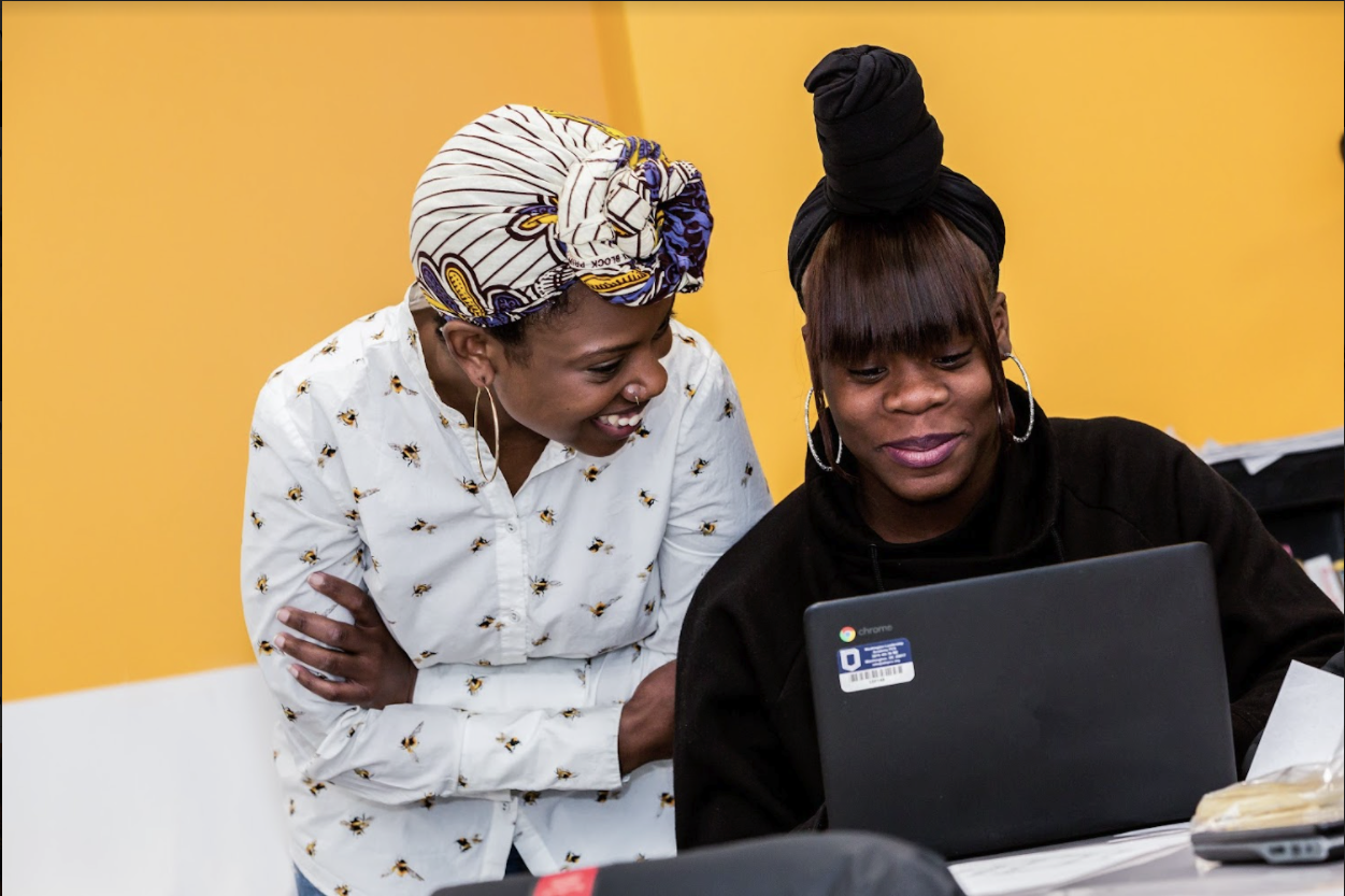 A teacher and a student looking at a computer screen and smiling. 