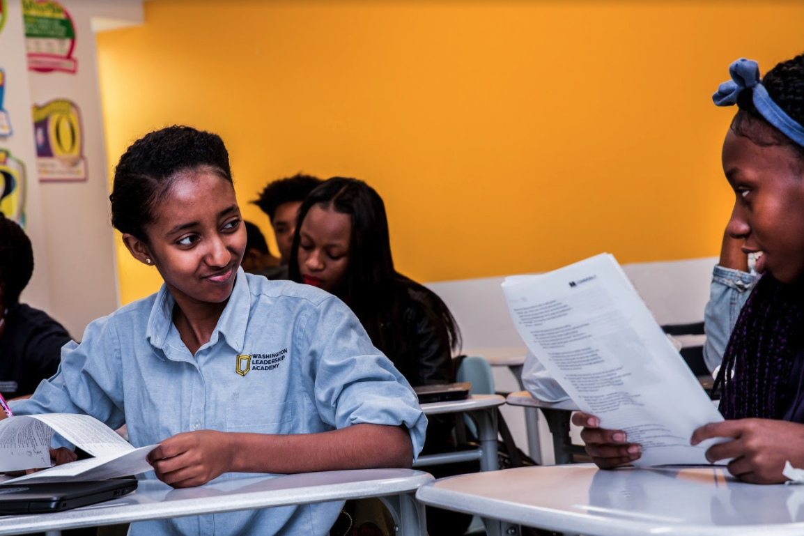 Two students sitting at desks and looking at each other. 