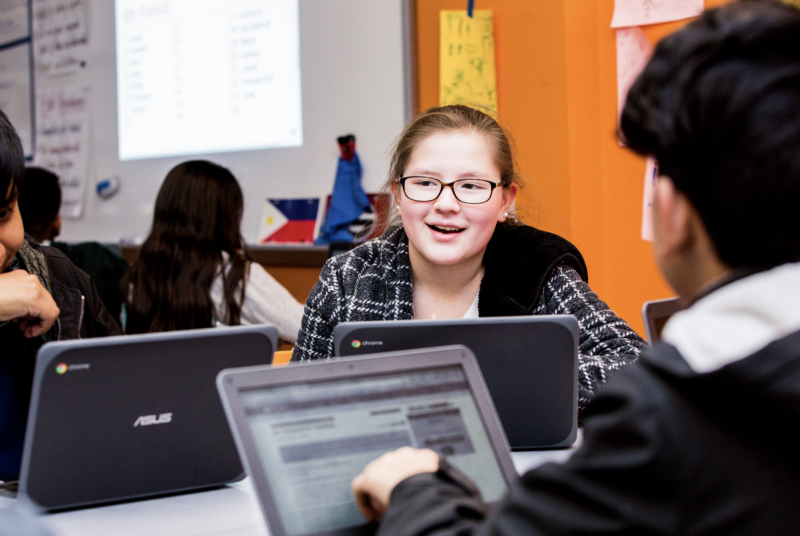 A student looking up while two other students work on their computers. 