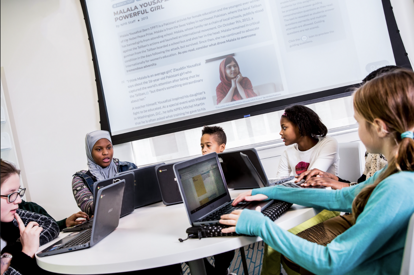 A group of students sitting at a round table and looking at each other. 